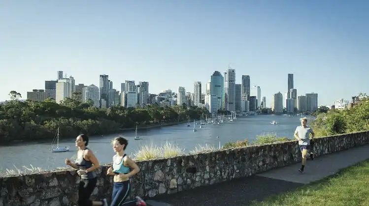 Futók a brisbane-i Kangaroo Point Cliffs sétányán, a folyóparti panorámával és a modern belvárosi felhőkarcolókkal a háttérben, napos időben.