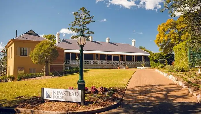 A brisbane-i Newstead House gyarmati stílusú, verandás történelmi épülete gondozott kerttel és klasszikus bejárati táblával, napos környezetben.